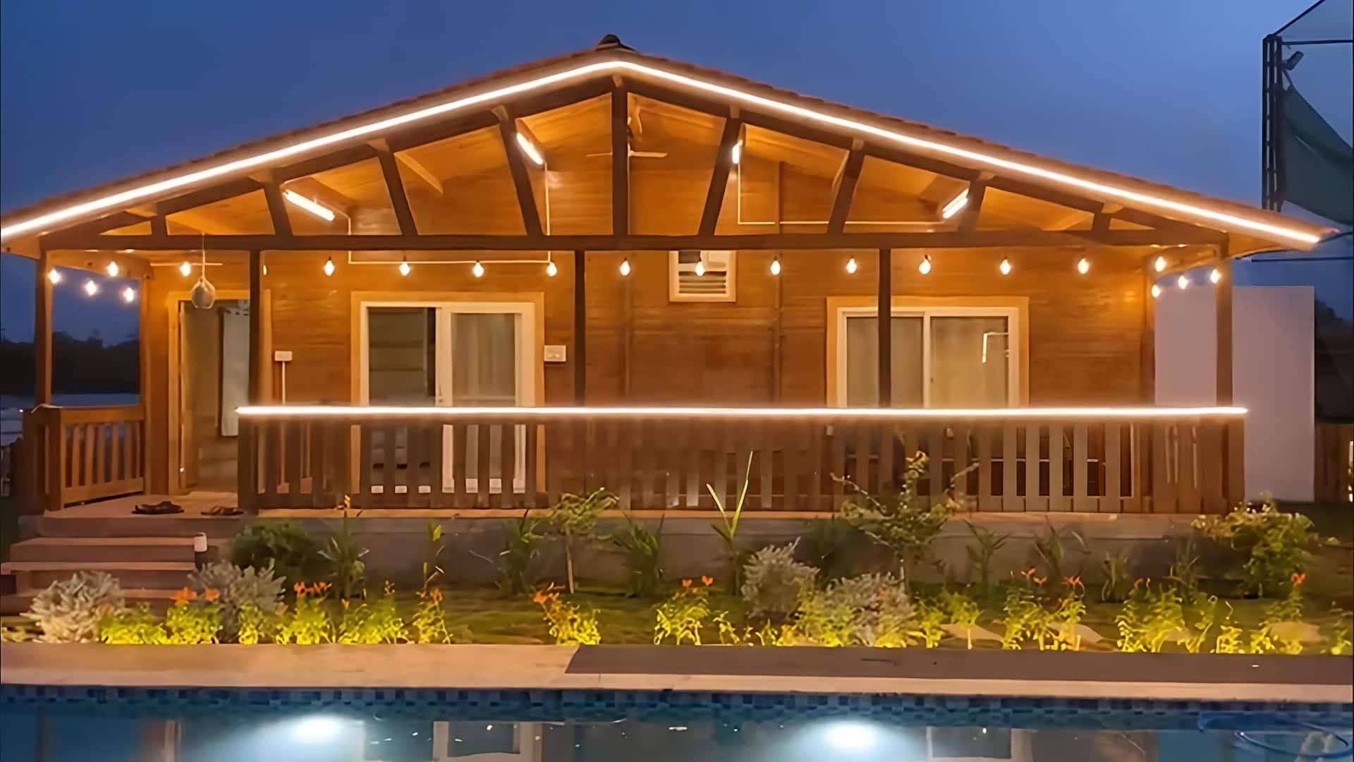 Cottage lit by string lights above the pool at night