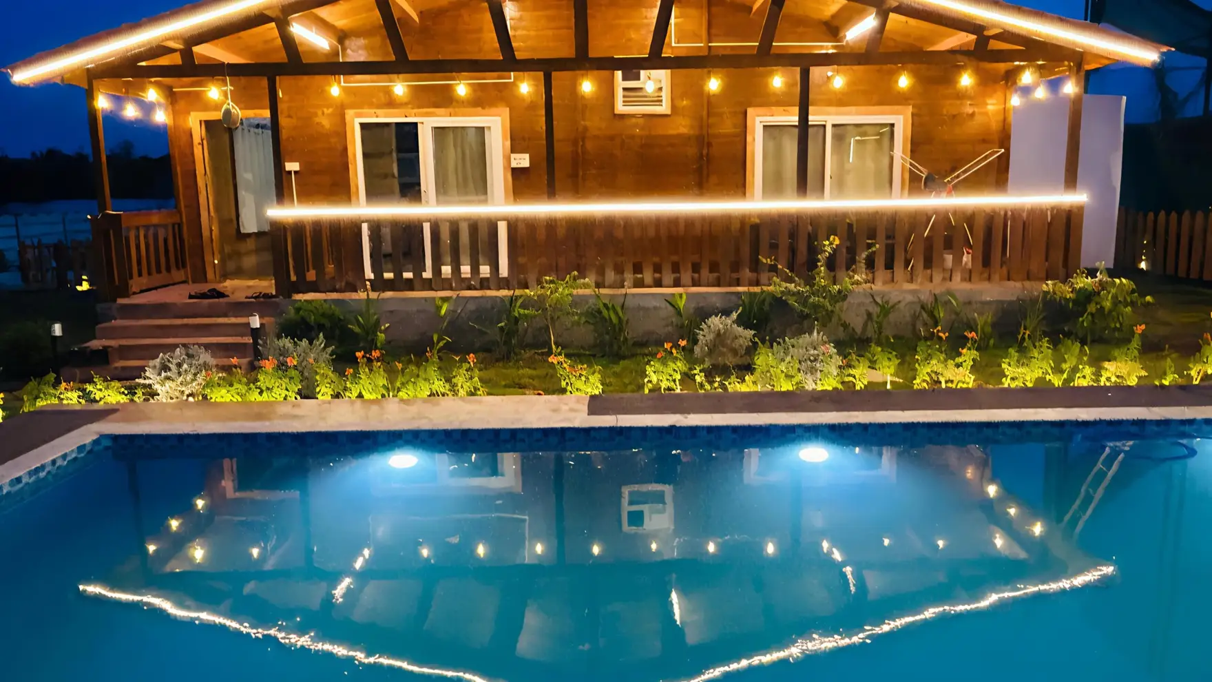 Wooden cottage lit up at night above the pool at AV Holistays