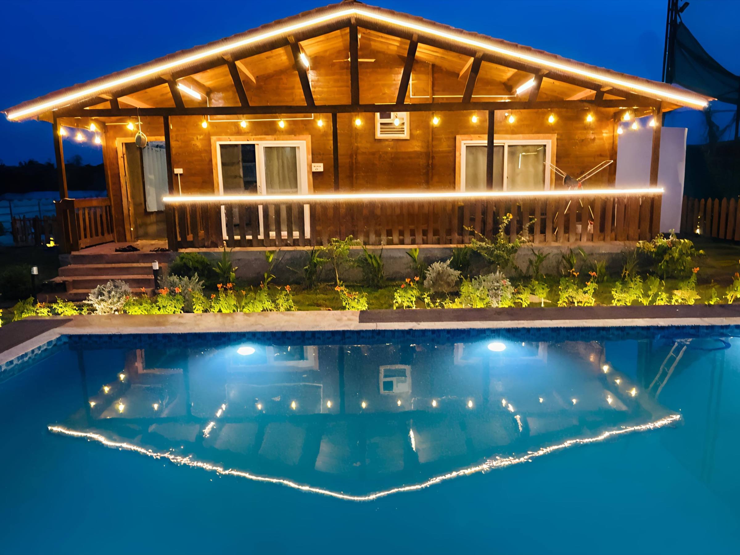 Ananta cottage lit by string lights, reflected in the pool at dusk